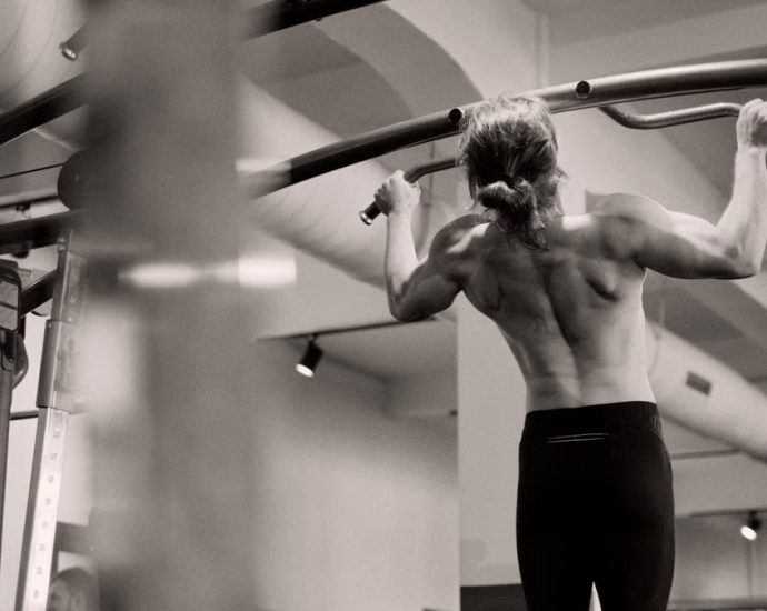 Focused on a man doing pull-ups in a gym, showcasing strength and fitness.