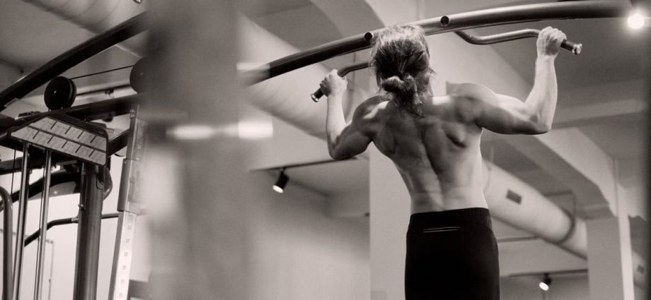 Focused on a man doing pull-ups in a gym, showcasing strength and fitness.